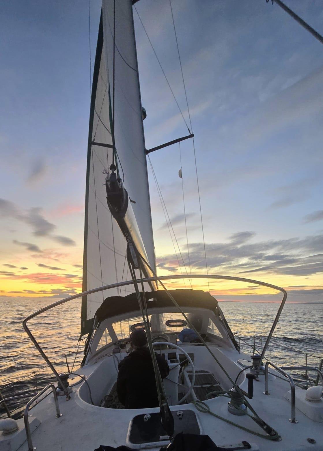 The Calma under sail at twilight, helmsman at the wheel